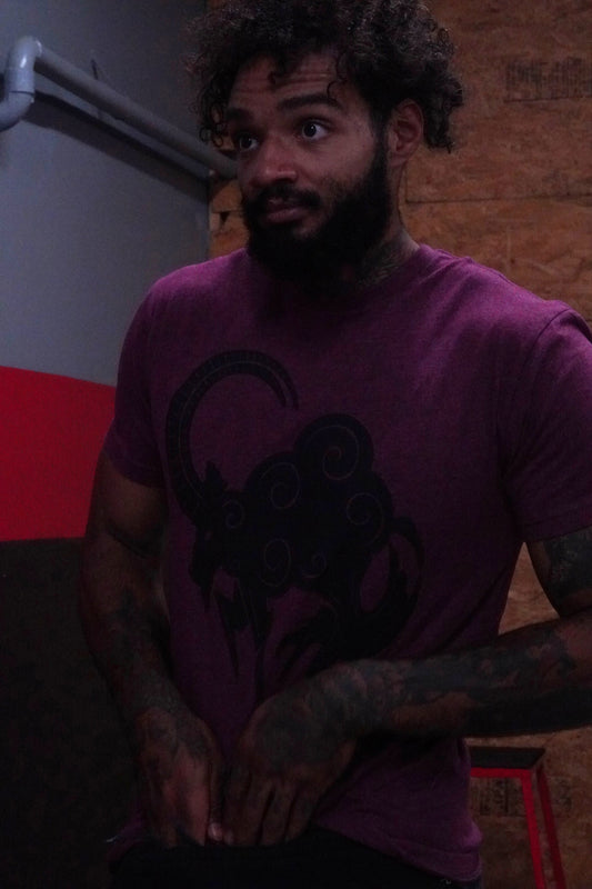 Man wearing a blood red t-shirt with a graphic design, standing against a red and gray wall.